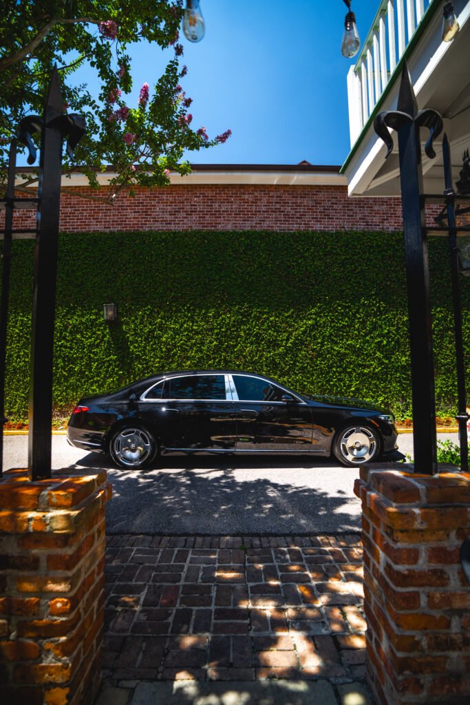 "Luxurious black car parked in front of a modern building with greenery in the foreground."
